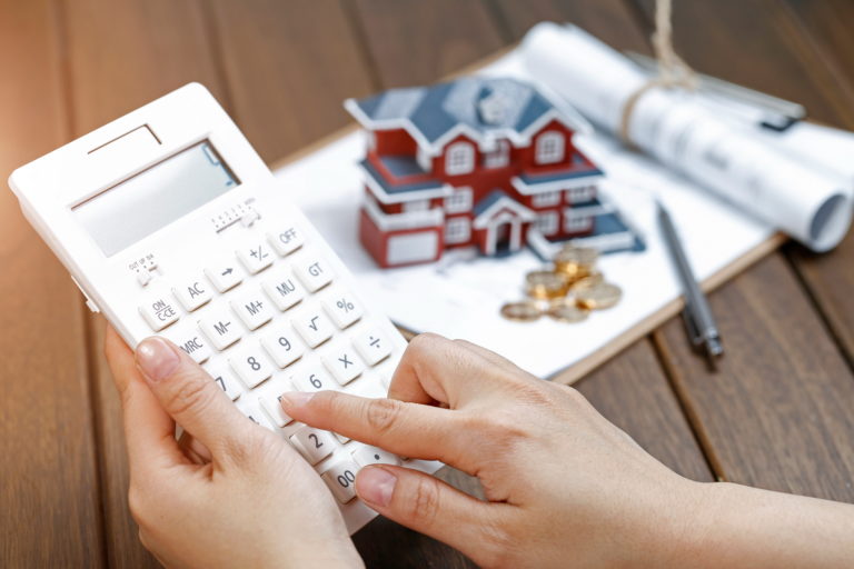 Refinance Your Mortgage - A female hand operating a calculator in front of a Villa house model